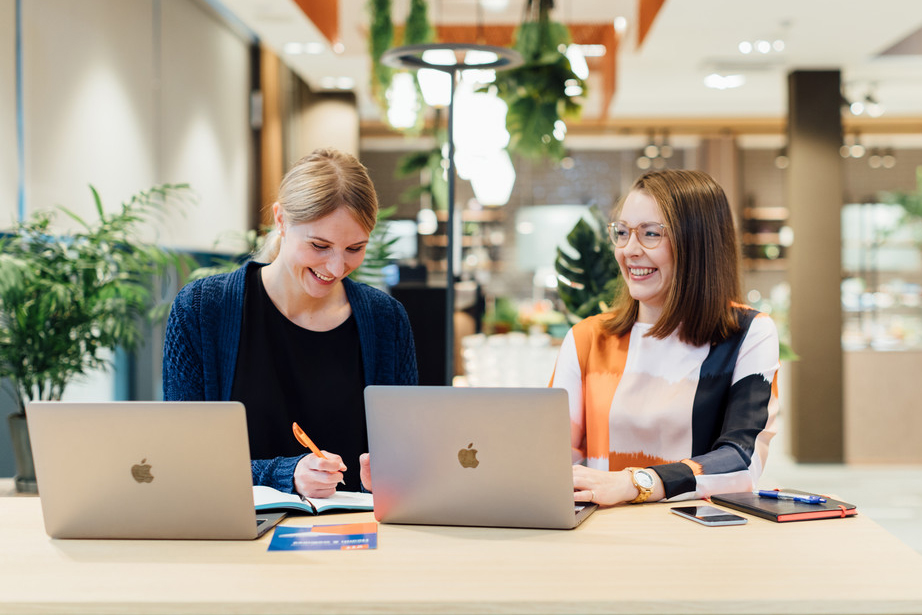 Women sitting in cafeteria with laptops and brochures